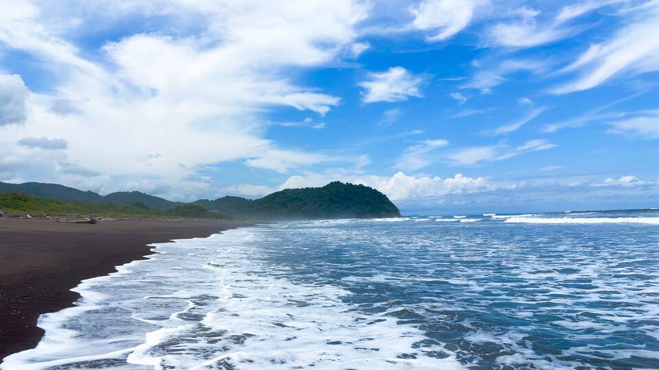 A beach with waves, a distant island, and a clear sky.