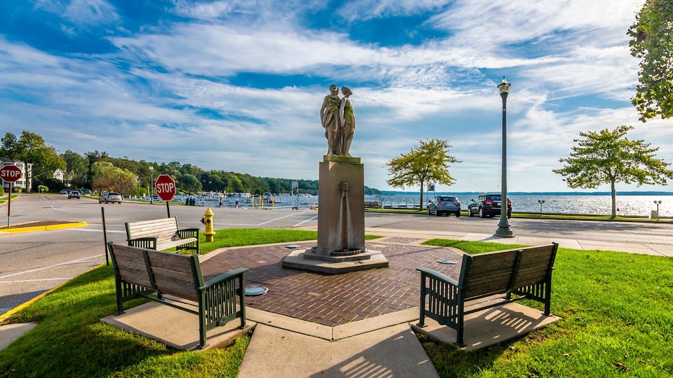 A park with benches, a statue, a stop sign, and a view of the water.