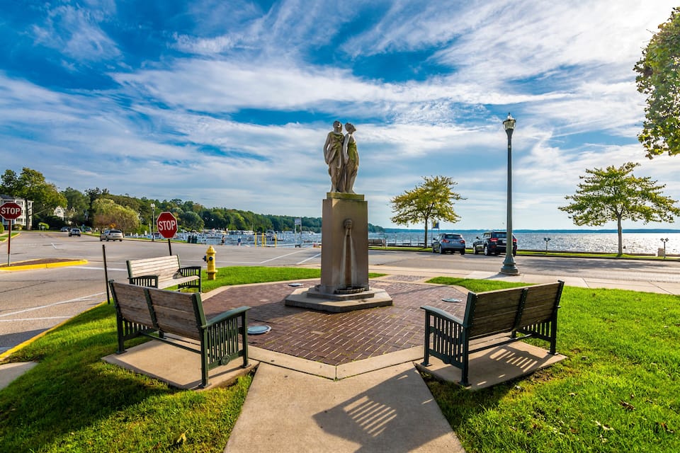 A park with benches, a statue, a stop sign, and a view of the water.