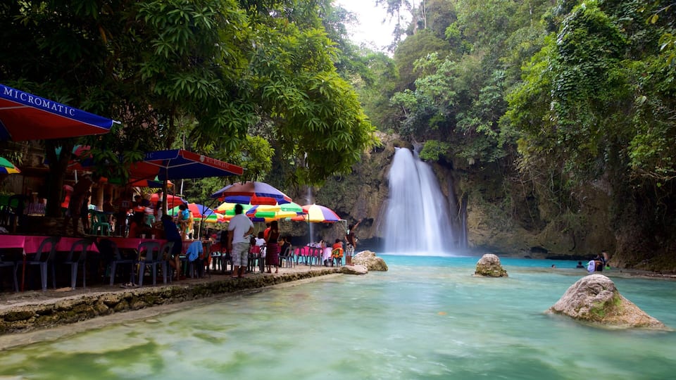 A waterfall, a pool of water, and a restaurant with colorful umbrellas.