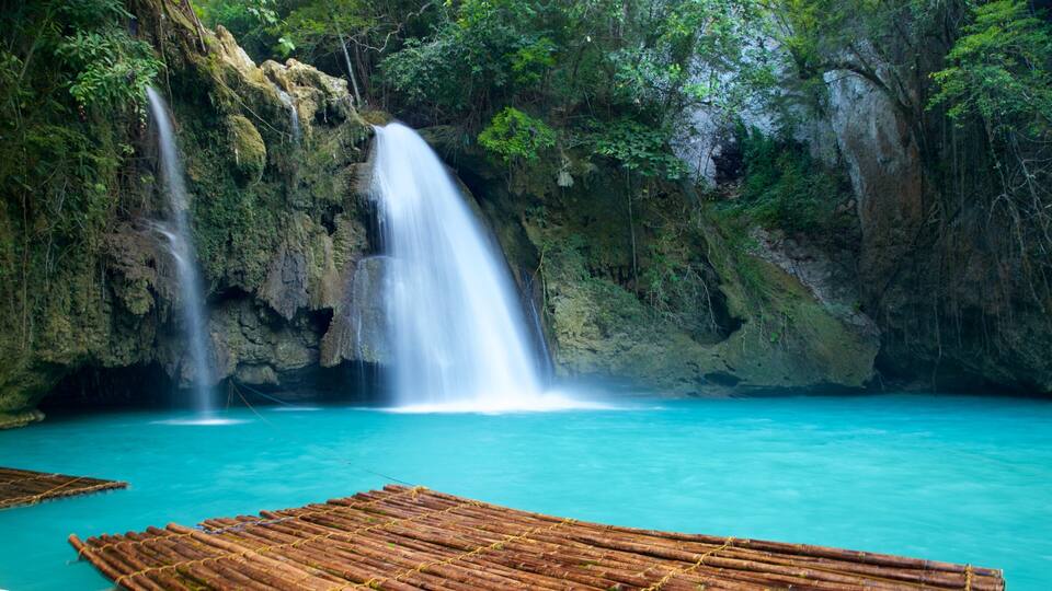 A waterfall in a lush forest with clear turquoise water.