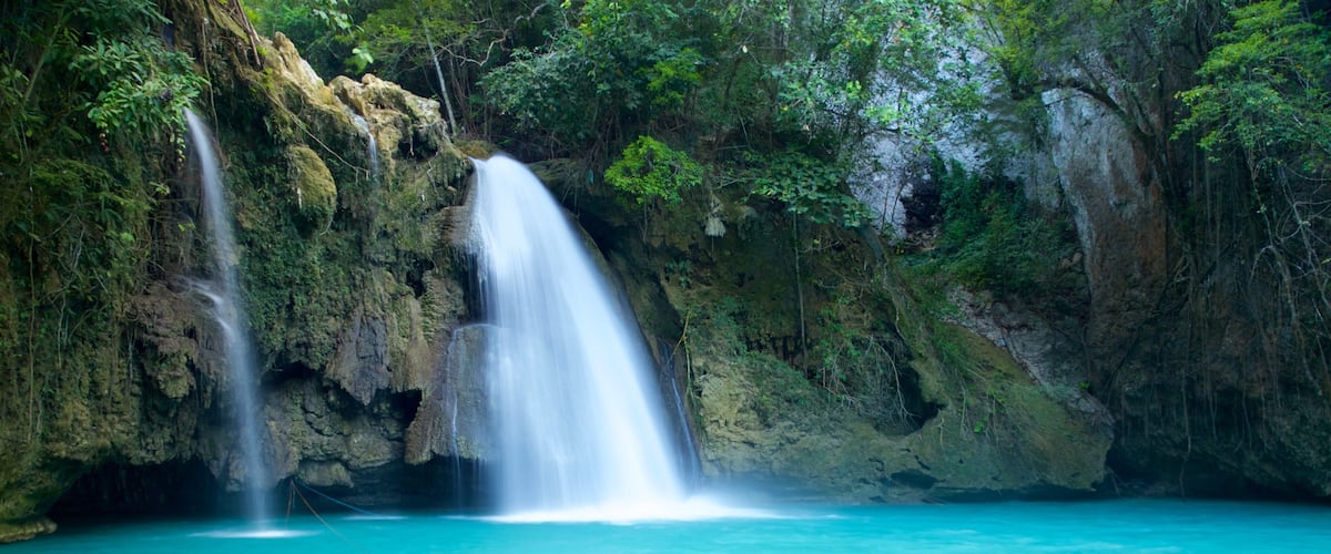 A waterfall in a lush forest with clear turquoise water.