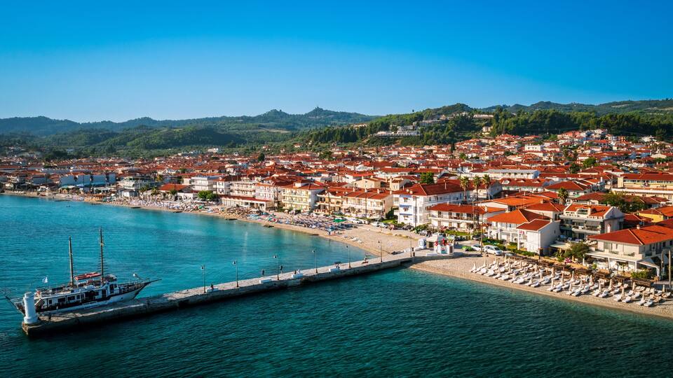 A coastal town with a marina, beach, and red-roofed buildings.