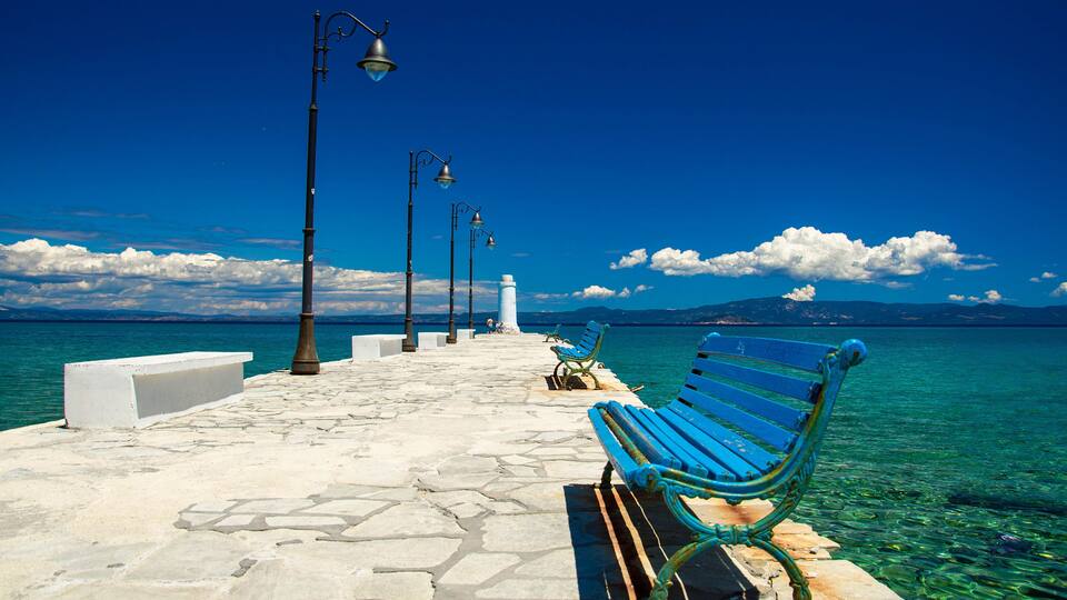 A stone pier with benches and street lamps overlooking a clear blue sea.