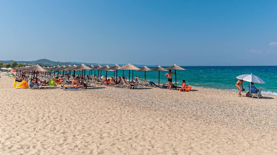 A beach with umbrellas, lounge chairs, and people relaxing by the water.