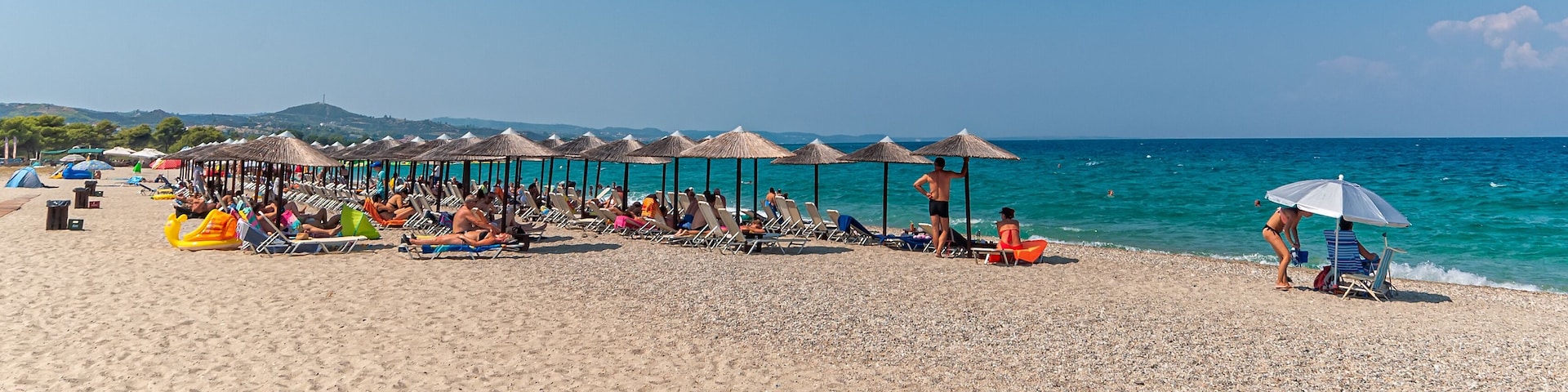Una playa con sombrillas, sillas de descanso y gente relajándose junto al agua.