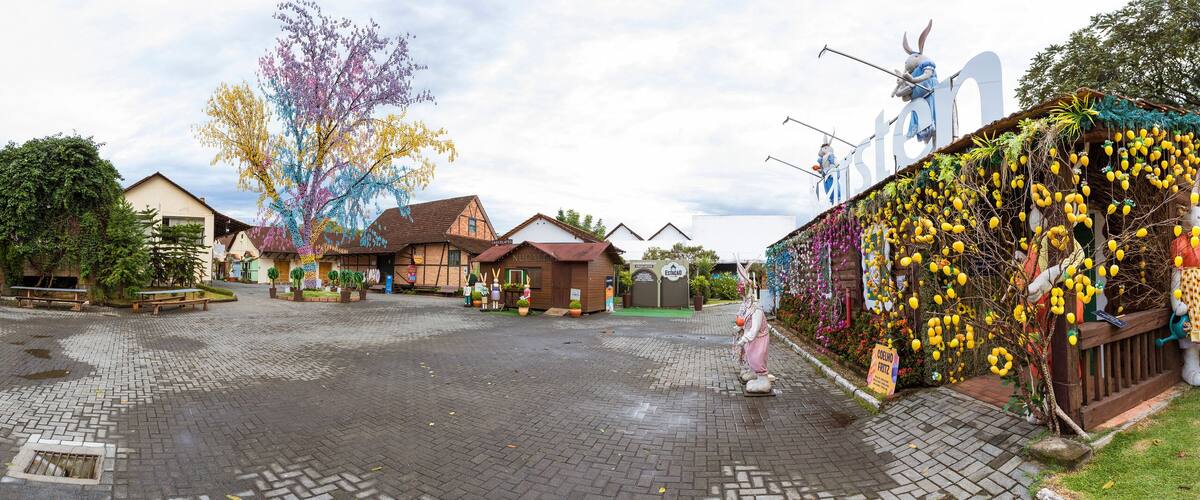 A cobblestone plaza with wooden benches, a covered seating area, and a colorful tree.