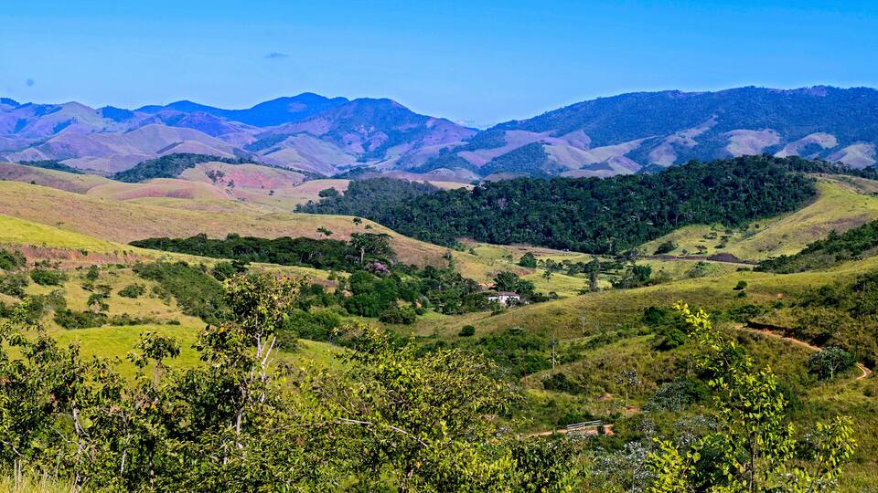 Rolling hills, a small white building, and distant mountains under a clear sky.