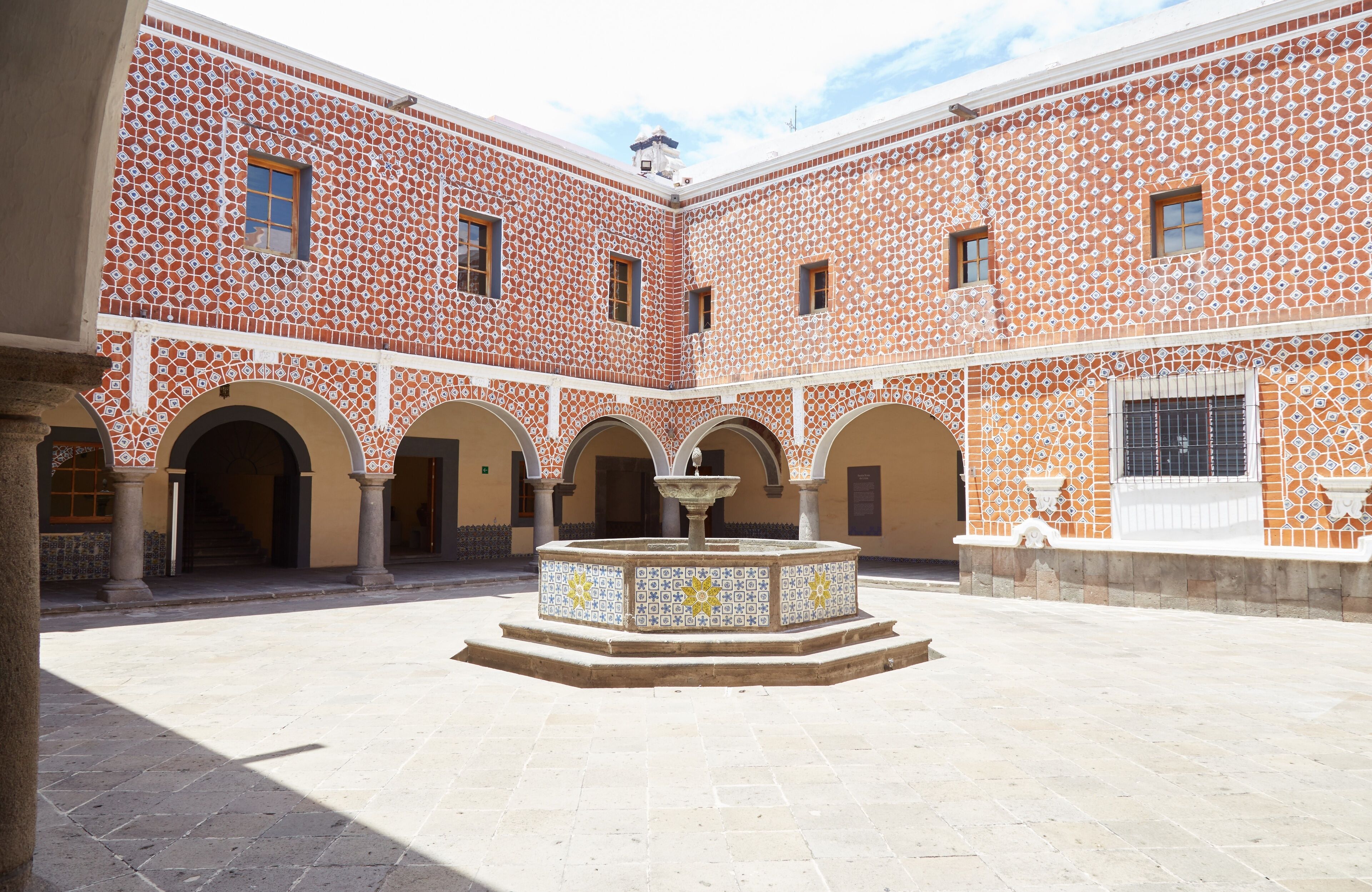 A courtyard with patterned walls, arches, and a central fountain.