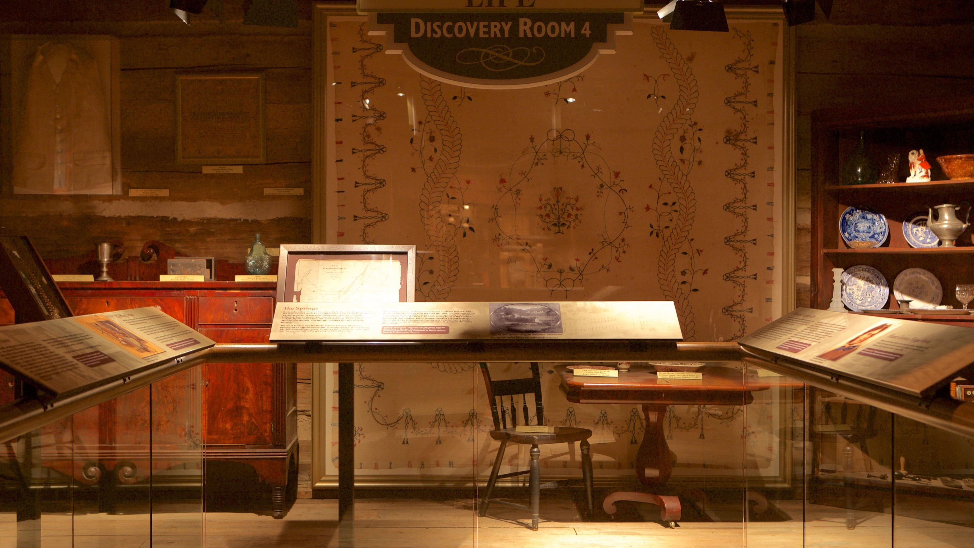 A museum exhibit with a wooden table, chairs, and a display case containing artifacts.