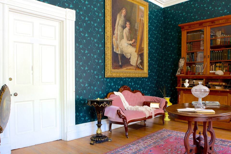 A room with a white door, a pink sofa, a wooden bookcase, and a painting on the wall.
