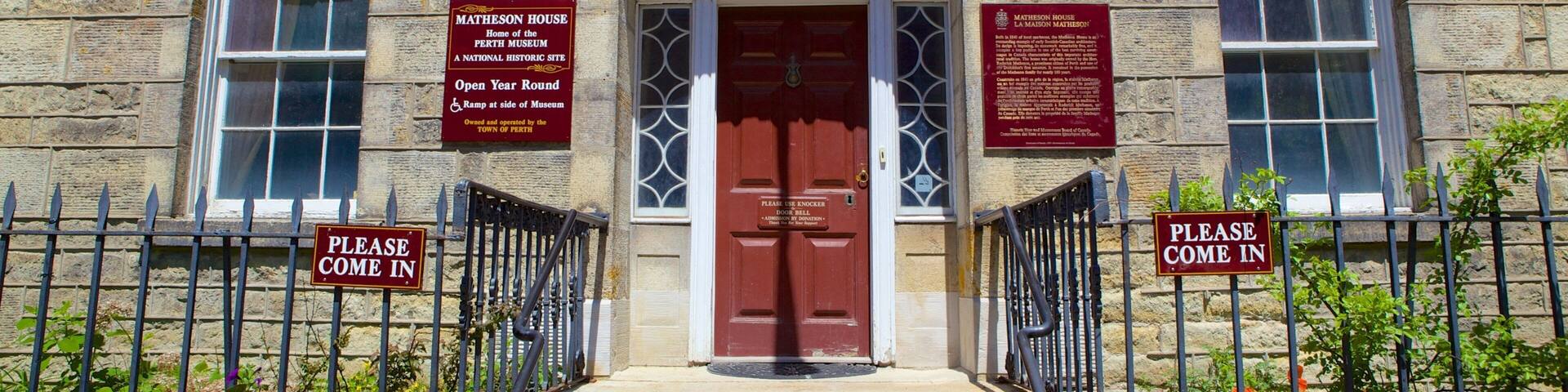 A historic building with a red door, stone walls, and signs indicating it is the home of the Perth Museum.