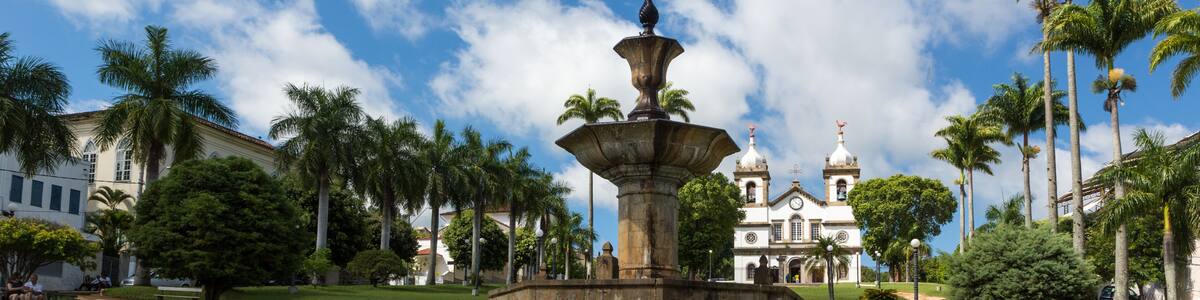 A fountain with multiple tiers, palm trees, and a building with domes in the background.
