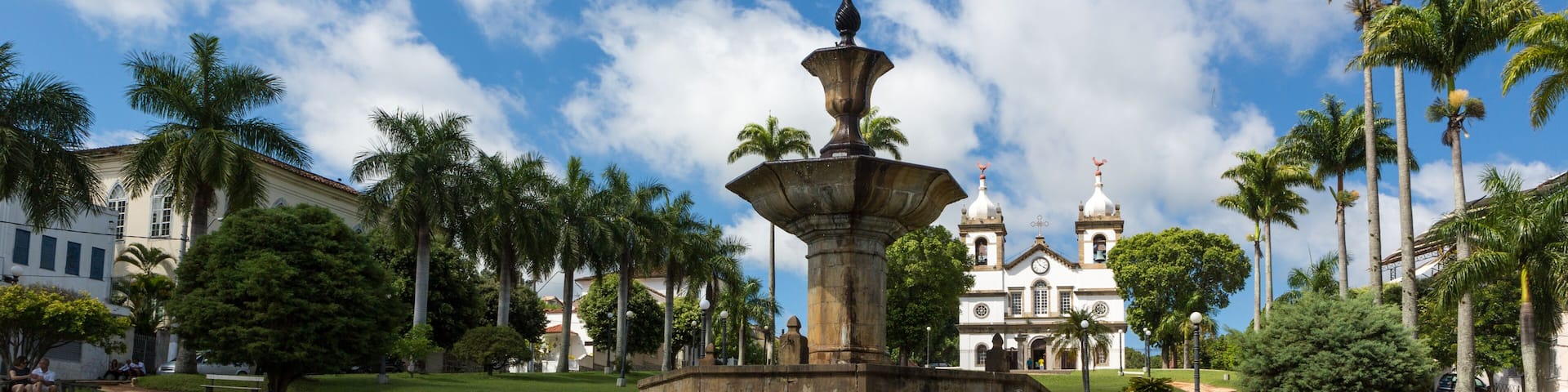 A fountain with multiple tiers, palm trees, and a building with domes in the background.