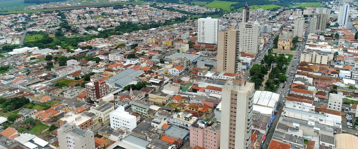 A densely populated urban area with a mix of high-rise and low-rise buildings, surrounded by green fields and distant hills.