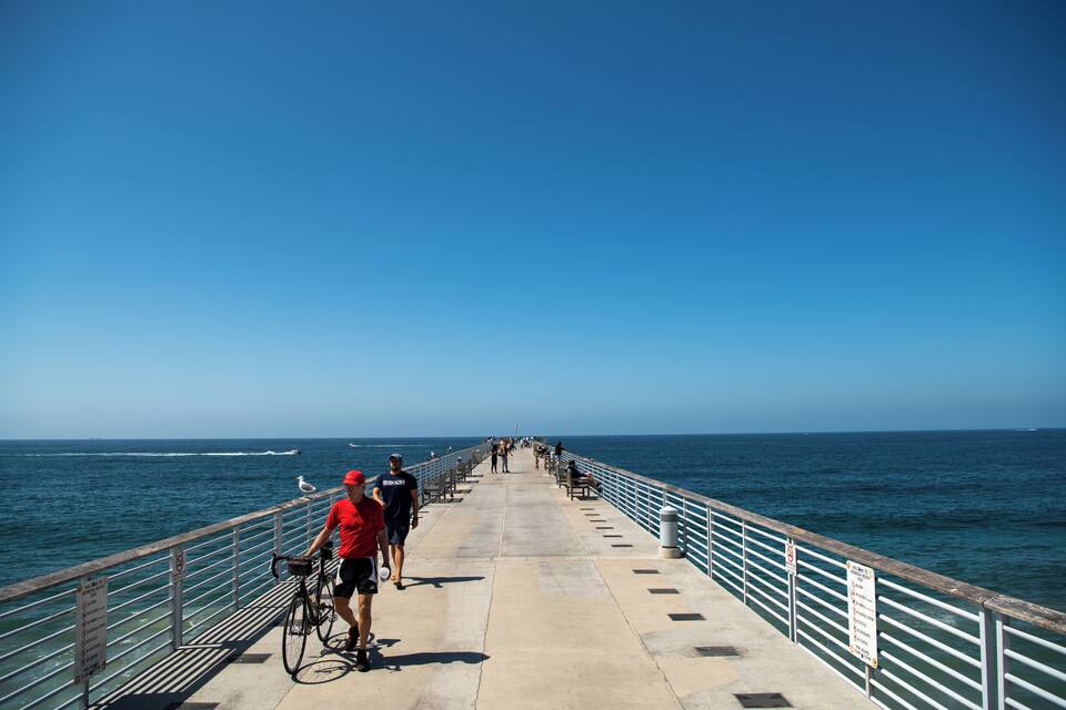 Une jetée qui s’avance dans l’océan, où l’on peut voir des gens se promener et faire du vélo.