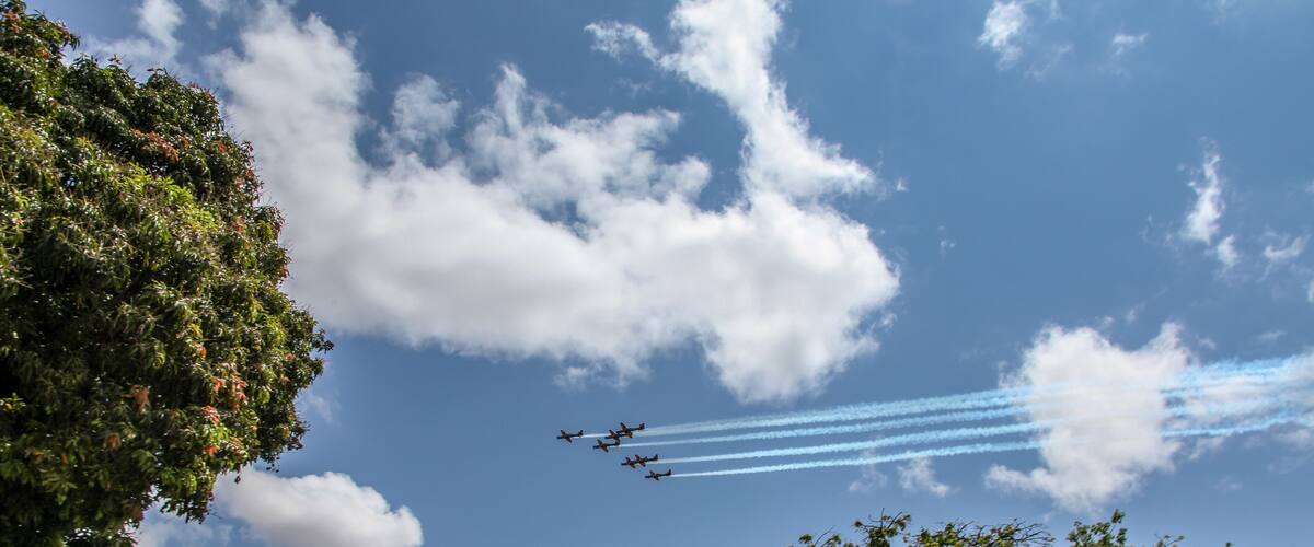 A clear blue sky with scattered clouds and a formation of aircraft leaving contrails.
