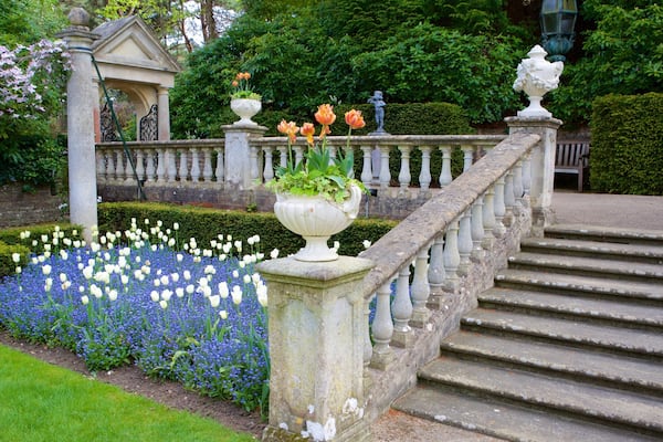 Ein Garten mit einer Steintreppe, weißen und blauen Blumen und Statuen.