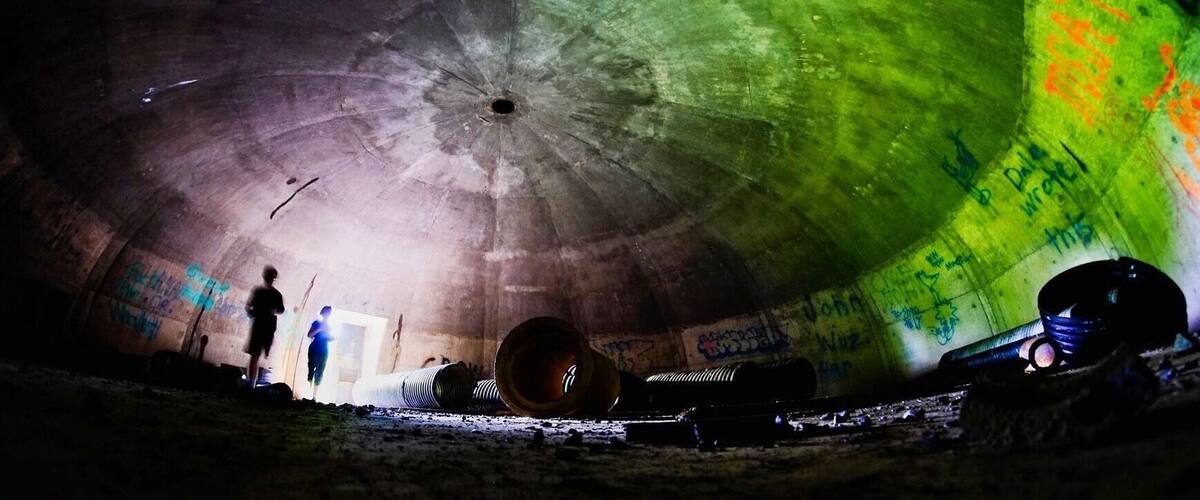 A dimly lit underground tunnel with graffiti on the walls and a person standing near a doorway.