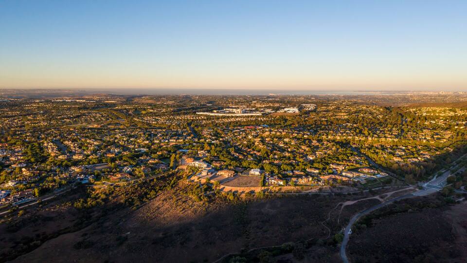 An aerial view of a densely populated city with a mix of residential and commercial buildings, surrounded by greenery and a clear sky.
