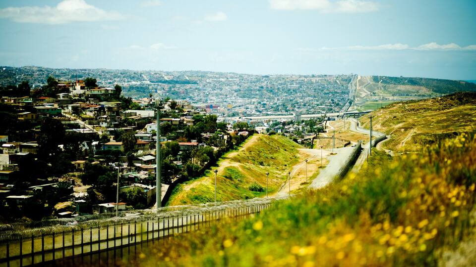 A hillside town with a winding road, a bridge in the distance, and a river in the foreground.