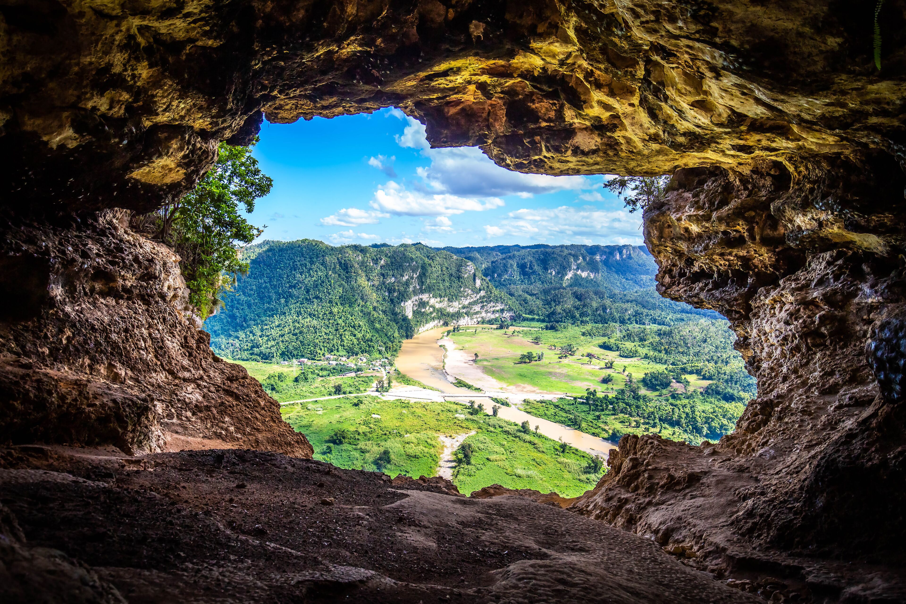 A cave opening with a view of a river and green hills.