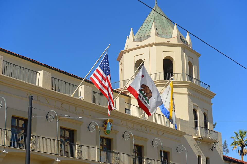 A building with a clock tower, American and Mexican flags, and a clear blue sky.