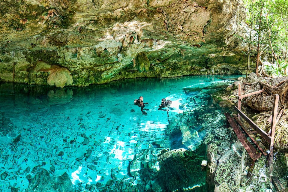 Una piscina blava i cristal·lina amb parets de roca, envoltada de vegetació exuberanta.
