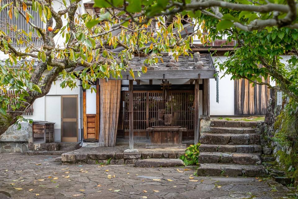 Um edifício japonês tradicional com entrada de madeira, degraus de pedra e um muro de pedra.