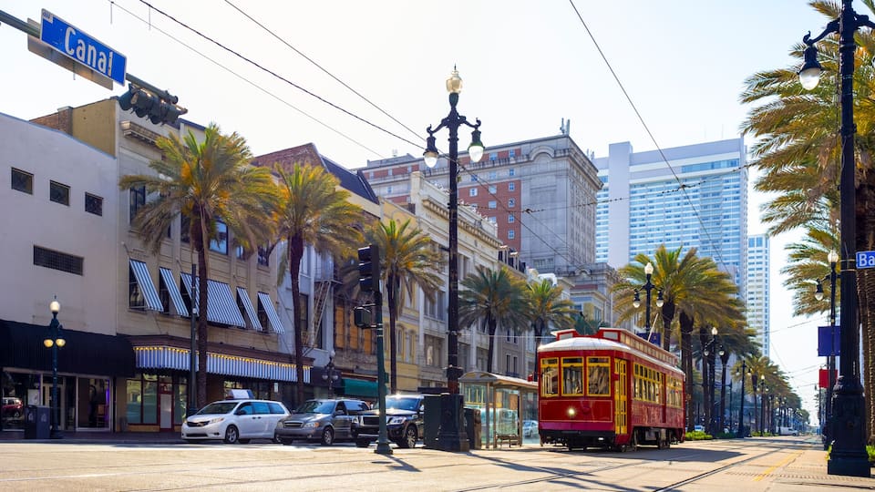 A street with a red trolley, palm trees, and buildings with striped awnings.
