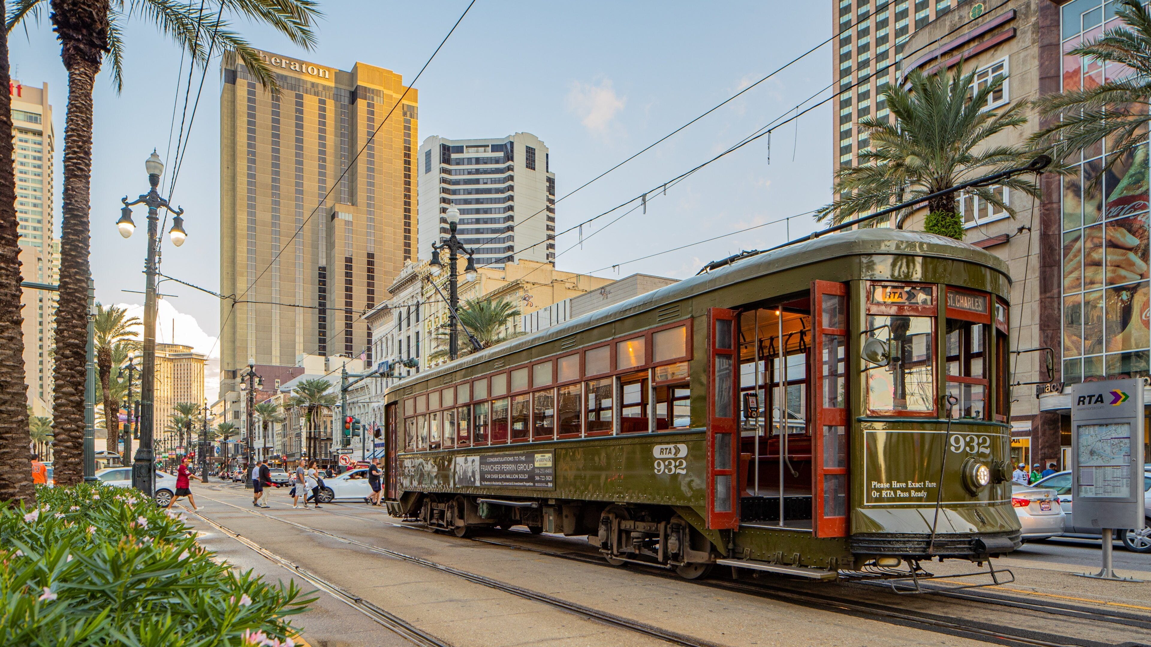 A vintage tram on tracks in an urban setting with tall buildings and palm trees.