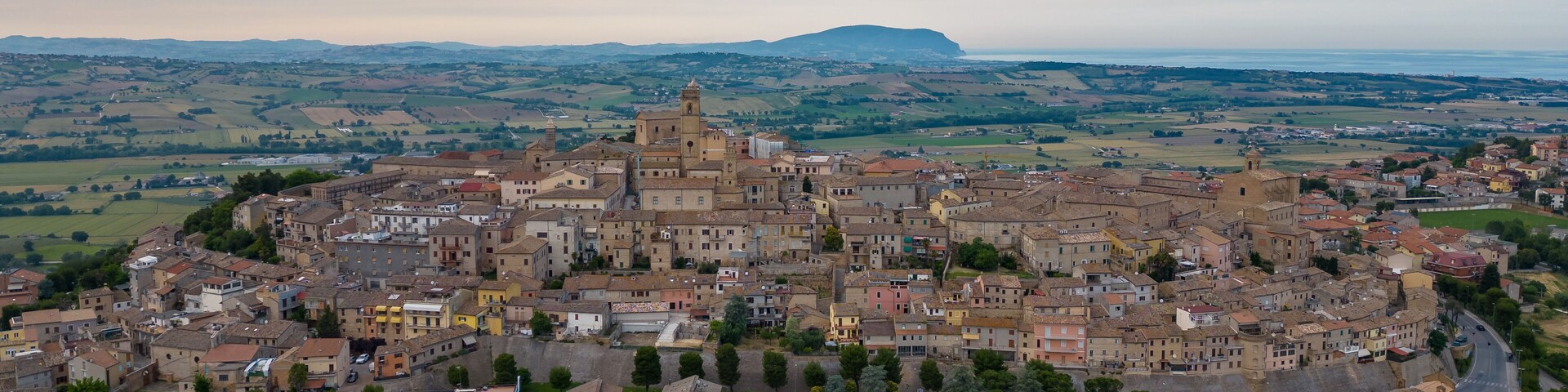 Vista aérea de un pueblo histórico con una iglesia destacada, rodeado de colinas ondulantes y campos.