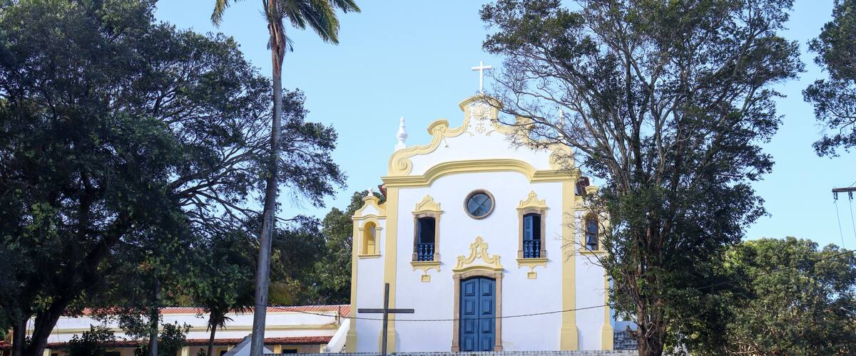 A small church with a blue door and a cross on top, surrounded by trees.