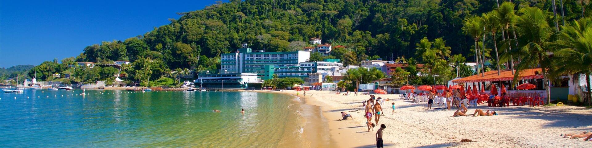 A beach with clear turquoise water, a sandy shore, and a backdrop of lush green hills.