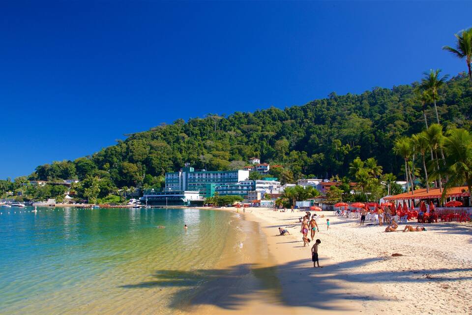 A beach with clear turquoise water, a sandy shore, and a backdrop of lush green hills.