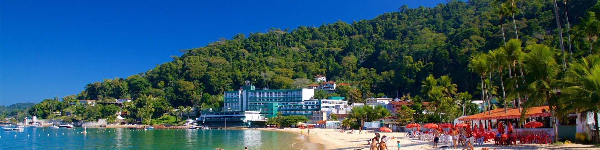Uma praia com águas turquesa cristalinas, uma faixa de areia e colinas verdes exuberantes ao fundo.