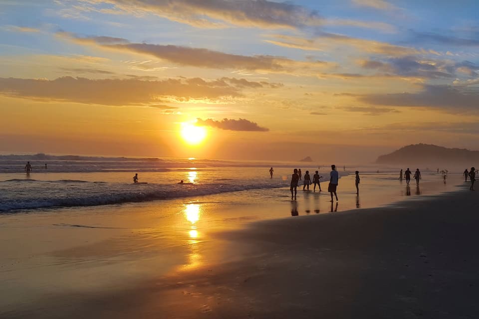 Una platja al capvespre, amb persones passejant al llarg de la riba.