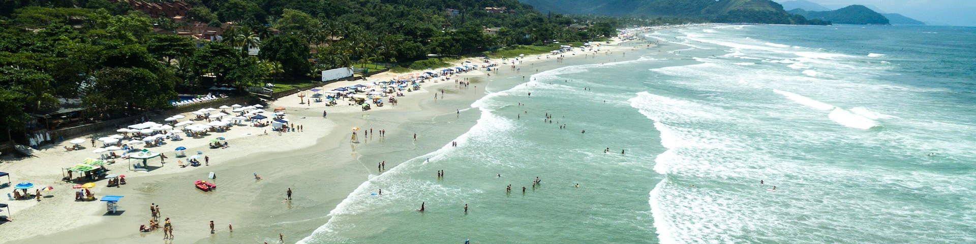 Una playa con gente nadando y tomando el sol, rodeada de colinas y montañas verdes y exuberantes.
