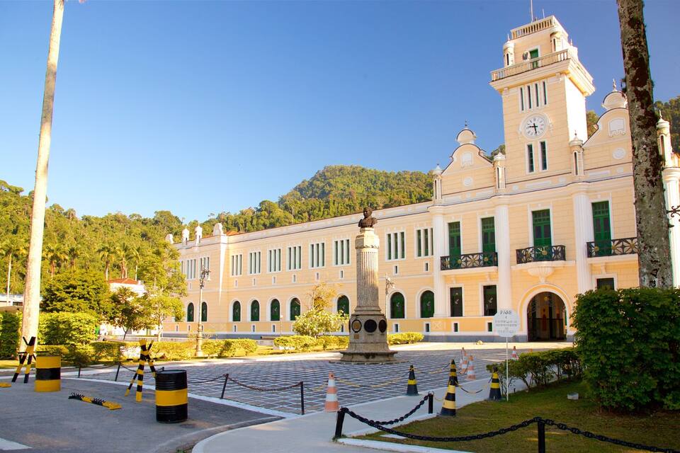 A historic building with a clock tower, surrounded by greenery and a paved area with traffic cones.