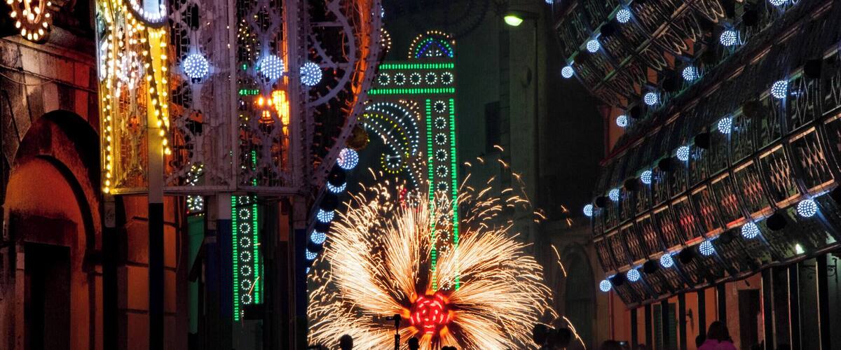A nighttime street with illuminated buildings, a Ferris wheel, and fireworks.