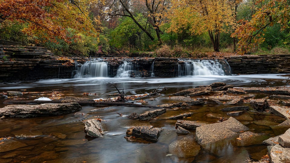 A waterfall cascading over a rocky ledge surrounded by autumn foliage.