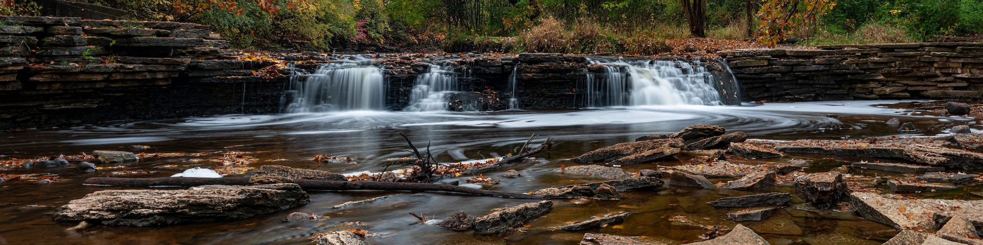 A waterfall cascading over a rocky ledge surrounded by autumn foliage.