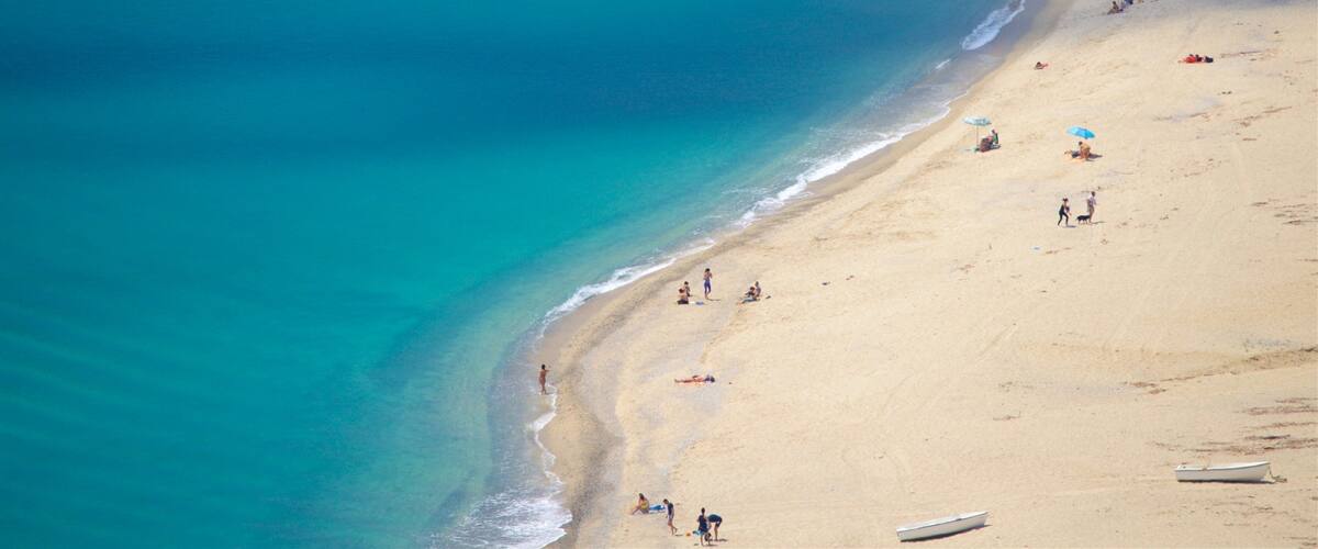 A beach with clear turquoise water, sandy shore, and a few boats.