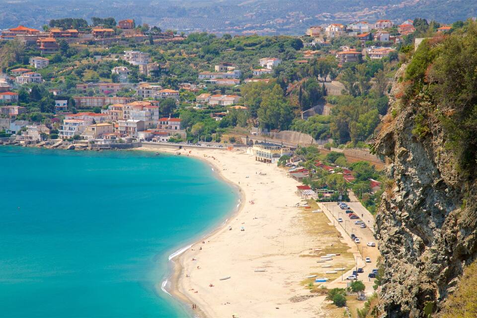 A coastal town with a sandy beach, a rocky cliff, and buildings with red roofs.