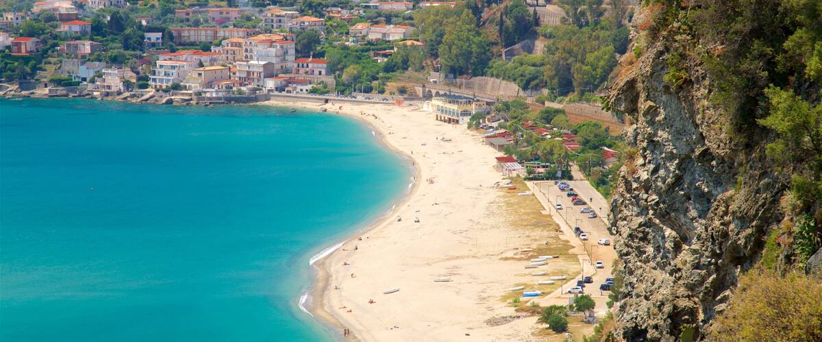 A coastal town with a sandy beach, a rocky cliff, and buildings with red roofs.