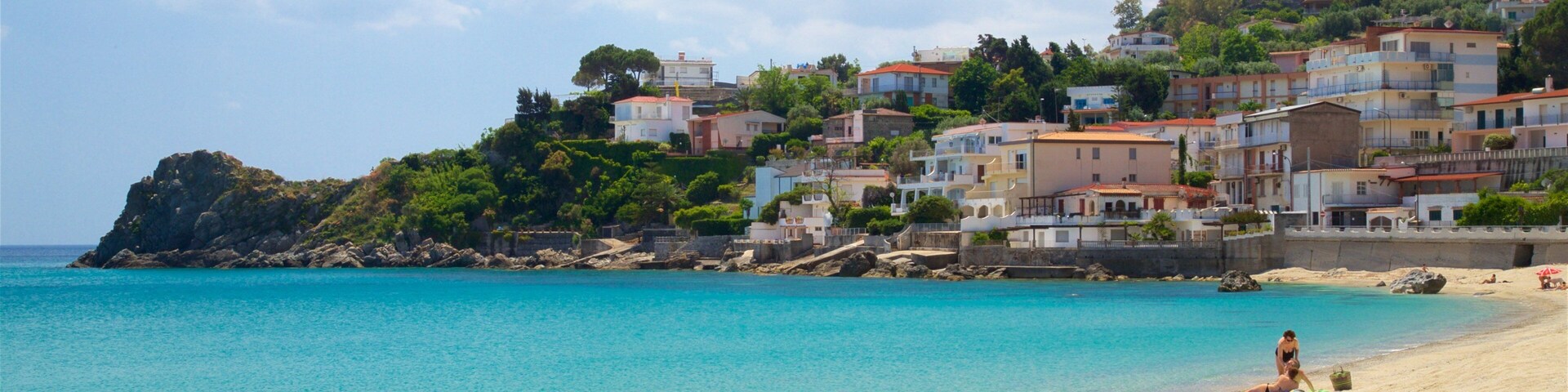 Una playa con agua turquesa cristalina, una orilla arenosa y una colina con edificios de colores.