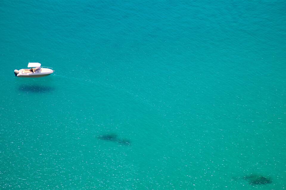 Um pequeno barco flutuando em águas turquesa, com alguns peixes visíveis abaixo da superfície.