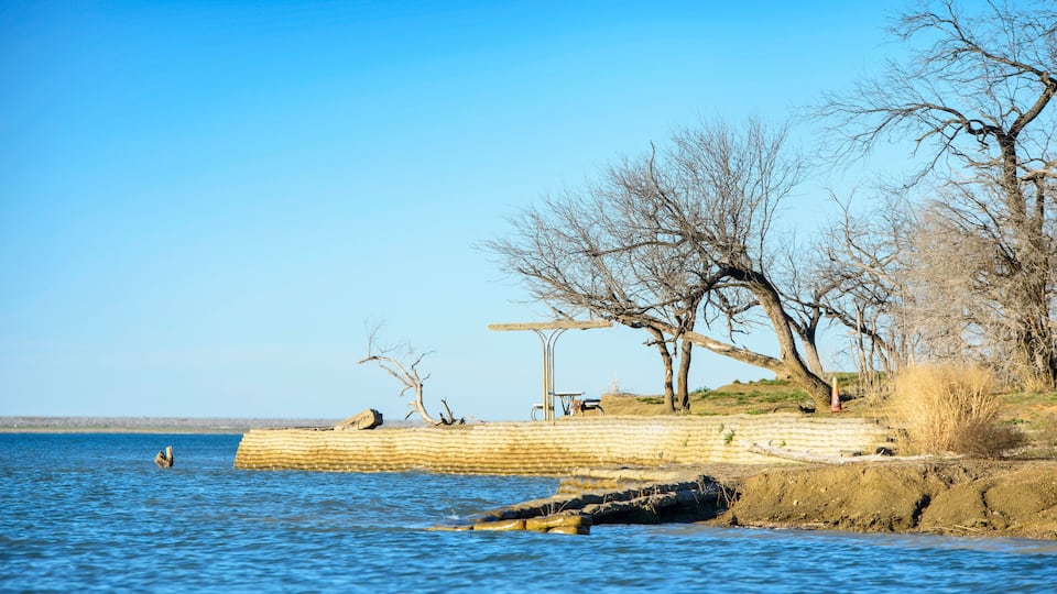 A calm river with a wooden pier and leafless trees along the bank.