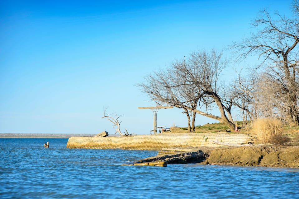 A calm river with a wooden pier and leafless trees along the bank.