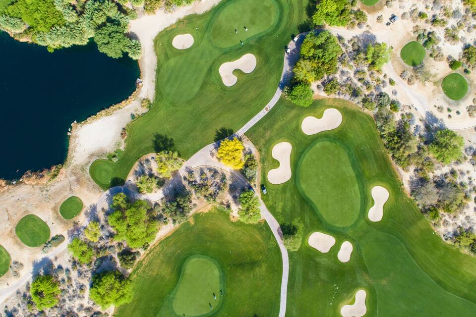Vue aérienne d’un parcours de golf avec des bunkers de sable, des plans d’eau et une végétation luxuriante.